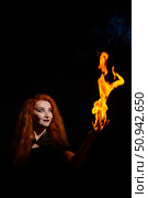 An ominous witch with long curly hair holds a magical fire. Tongues of flame on the palms of a red-haired smirking woman. Witchcraft. Стоковое фото, фотограф Михаил Решетников / Фотобанк Лори