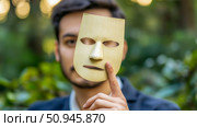 Concept: Masking Identity: Man holding a blank paper mask in front of his face, partially concealing his identity in an outdoor setting. Стоковое AI-изображение, AI-художник Данила Большаков / Фотобанк Лори