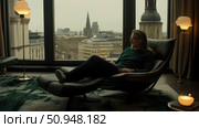 Thoughtful Moment: A Man Relaxing in Chair with City Glimpse, Indoor Serenity and Urban Reflection. Стоковое AI-изображение, AI-художник Данила Большаков / Фотобанк Лори