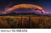 Dramatic landscape with distant mountain range under a stormy sky and lightning strikes, viewed through a rustic wooden fence on a grassy plain. Стоковое AI-изображение, AI-художник Данила Большаков / Фотобанк Лори