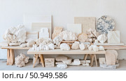 Mineral Collection Arrangement: A showcase of geological specimens and stone samples on a table against a textured white wall. Стоковое AI-изображение, AI-художник Данила Большаков / Фотобанк Лори