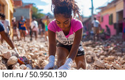 A resilient young woman diligently sifting through earthquake rubble during a community cleanup effort under bright sunshine, symbolizing hope and recovery. Стоковое AI-изображение, AI-художник Данила Большаков / Фотобанк Лори
