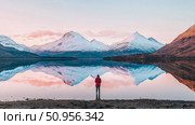 Winter Serenity: Solitary human figure contemplating a breathtaking mountain panorama mirrored in tranquil lake waters at soft dawn or dusk, a scenic travel expedition. Стоковое AI-изображение, AI-художник Данила Большаков / Фотобанк Лори