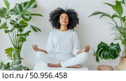 Tranquil moment: An African woman practices mindful meditation in a pristine setting surrounded by vibrant houseplant foliage for inner calm. Стоковое AI-изображение, AI-художник Данила Большаков / Фотобанк Лори
