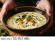 Hands expertly ladle creamy salmon soup into a rustic bowl, showcasing culinary craftsmanship. The rich broth envelops tender fish and vegetables for an enticing meal experience. Стоковое AI-изображение, AI-художник Nart / Фотобанк Лори