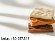 A detailed close-up of stacked chocolate bars showcases the distinct layers of white, milk, and dark chocolate. The intricate textures highlight the rich variety of this delicious treat. Стоковое AI-изображение, AI-художник Nart / Фотобанк Лори