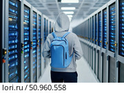 Person in hoodie with backpack walks through a server room filled with glowing data racks, symbolizing cybersecurity, hacking, technology access, or digital intrusion in progress. Стоковое AI-изображение, AI-художник Катерина Бондарец / Фотобанк Лори