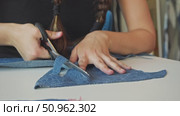 A young lady in a sewing studio meticulously snips a denim fabric into segments using scissors. Стоковое видео, видеограф Strunov David / Фотобанк Лори