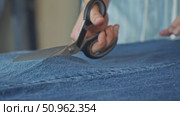 tailor's hands, wielding scissors, as they trim a blue denim fabric along a seam in a workshop. Стоковое видео, видеограф Strunov David / Фотобанк Лори