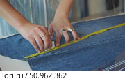 Hands placing measuring tape on denim cloth for cutting markings. Стоковое видео, видеограф Strunov David / Фотобанк Лори