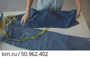 Using measuring tape, seamstress works at her table and calculates length of denim fabric she will need to work with for jeans. Стоковое видео, видеограф Strunov David / Фотобанк Лори