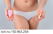A faceless woman in cotton panties holds a pink menstrual cup and tampon on a white background. Various hygiene products during menstruation. Стоковое фото, фотограф Михаил Решетников / Фотобанк Лори