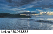 Early morning. The ocean waves are foaming and spreading across the beach. The clouds in the blue sky are illuminated with golden light. A hill in the distance. Malaysia. Borneo. Kota Kinabalu. Стоковое фото, фотограф Вера Ивановна Кубарева / Фотобанк Лори