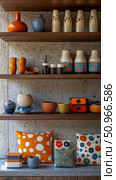 A colorful and eclectic home decor collection displayed on wooden shelves against a concrete wall, showcasing various ceramic vases, bowls, and patterned cushions for modern interior living inspirati. Стоковое AI-изображение, AI-художник Данила Большаков / Фотобанк Лори