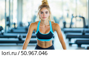 Fit young woman with blonde hair and blue eyes ready for a challenging workout session in a bright gymnasium. Стоковое AI-изображение, AI-художник Данила Большаков / Фотобанк Лори