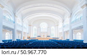 A majestic architectural interior of a bright, pristine white assembly hall, featuring grand vaulted ceilings, elegant arches, and rows of empty blue seating, prepared for a formal event or solemn ga. Стоковое AI-изображение, AI-художник Данила Большаков / Фотобанк Лори