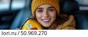 A cheerful young woman with captivating blue eyes, adorned in a vibrant yellow knitted beanie and a cozy winter jacket, smiles warmly while holding a heart-shaped object within the comfortable interior of a car, conveying joy and warmth on a journey. Стоковое AI-изображение, AI-художник Данила Большаков / Фотобанк Лори