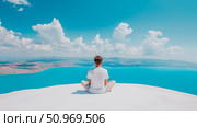 Peaceful solitude: a man in a meditative pose on a pristine white surface overlooks an expansive, vibrant turquoise lake and distant natural landscape under a serene blue sky with clouds. Стоковое AI-изображение, AI-художник Данила Большаков / Фотобанк Лори