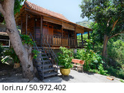 NHA TRANG, VIETNAM - APRIL 28, 2025. Wooden house under a tropical tree in Buddhist Hua Da Bao Monastery. Редакционное фото, фотограф Сергей Фролов / Фотобанк Лори