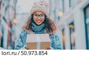 Joyful young woman with glasses and winter wear, brightly smiling while holding a package outdoors on a chilly day. Стоковое AI-видео, аниматор Данила Большаков / Фотобанк Лори