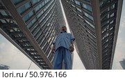 Low angle view of a determined laborer standing among towering modern buildings, illustrating the contrast between urban development and the social class divide. Стоковое AI-видео, аниматор Данил Руденко / Фотобанк Лори