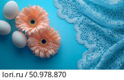 Pastel Gerbera Daisies, Eggs, and Lacy Fabric on a Blue Background: A Springtime Still Life. Стоковое AI-изображение, AI-художник Данила Большаков / Фотобанк Лори