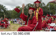 A gathering of individuals dressed in graduation gowns, standing together and joyously waving their hands in celebration. Стоковое AI-изображение, AI-художник Данила Большаков / Фотобанк Лори