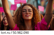 A young woman with curly hair and glasses joyfully participates in a demonstration, arms raised high. Стоковое AI-изображение, AI-художник Данила Большаков / Фотобанк Лори