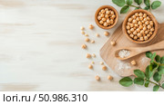 Fresh chickpeas in rustic wooden bowls with spoon of sea salt and green leaves on light wooden table, healthy cooking ingredients flat lay. Стоковое AI-изображение, AI-художник Данила Большаков / Фотобанк Лори