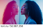 Captivating profile of modern woman with curly hair and reflective glasses mesmerized by her striking duotone reflection in vibrant, neon-lit digital space. Стоковое AI-изображение, AI-художник Данила Большаков / Фотобанк Лори