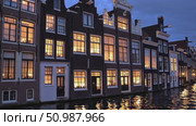 Candlelight glowing from windows casting soft reflections on tranquil waters, illuminating historic Amsterdam canal houses during twilight evening. Стоковое AI-видео, аниматор Данил Руденко / Фотобанк Лори