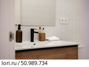 A modern bathroom with a sleek sink, black faucet, and wooden cabinet. The countertop holds a brown bottle, toothbrushes, and neatly folded towels. Стоковое фото, фотограф PAv / Фотобанк Лори