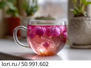 Pink flower tea brewing in glass cup on windowsill. Стоковое фото, фотограф Юрий Поздников / Фотобанк Лори