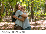 Tender embrace concept: Mother and son hugging tightly in a lush green forest environment filled with sunlight, conveying familial love and warmth. Стоковое фото, фотограф Данила Большаков / Фотобанк Лори