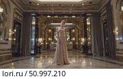 Elegant woman wearing a beautiful evening gown posing in a luxury hotel lobby with marble floor, golden decorations and sophisticated lighting. Стоковое AI-видео, аниматор Данил Руденко / Фотобанк Лори