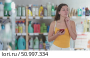 Thoughtful young girl in summer clothes scrolling smartphone while looking for some products in supermarket. Стоковое видео, видеограф Яков Филимонов / Фотобанк Лори