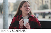 Girl with long hair is sitting in a street cafe with a cup of hot strong coffee. European woman stopped during a walk and drinks coffee. Стоковое видео, видеограф Яков Филимонов / Фотобанк Лори