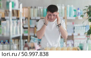 Guy in summer clothes is standing in a pharmacy and pulling his head. Young guy came to a European pharmacy for pills for headaches and migraines. Стоковое видео, видеограф Яков Филимонов / Фотобанк Лори