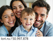 In a warm and inviting living room, a cheerful family poses with genuine smiles. The parents embrace their two young children, creating a lively atmosphere of love and happiness Generative AI. Стоковое AI-изображение, AI-художник Юлия Петровская / Фотобанк Лори