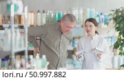 Senior man visits pharmacy and suffers from backache. Girl pharmacist offer help. Стоковое видео, видеограф Яков Филимонов / Фотобанк Лори