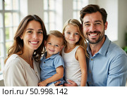 A cheerful family gathers together, with parents holding their two children tightly. Laughter fills the bright indoor area, celebrating love and togetherness in a cozy home Generative AI. Стоковое AI-изображение, AI-художник Юлия Петровская / Фотобанк Лори