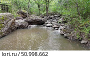 Flowing stream with clear water cascading over rocky terrain, surrounded by lush greenery and moss-covered stones, creating a serene natural landscape with tranquil ambiance. Стоковое видео, видеограф Ирина Ручушкина / Фотобанк Лори