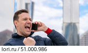 Portrait of handsome millennial man who received amazing news on phone, looking forward, clenching his fist in winners gesture and screaming yeah. Стоковое фото, фотограф Данила Большаков / Фотобанк Лори