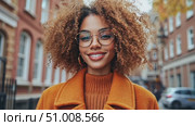A woman smiles brightly while wearing a stylish orange coat and standing on a picturesque city street surrounded by autumn colors. Стоковое AI-видео, аниматор Данила Большаков / Фотобанк Лори