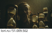 Mysterious figure observes sand timers in dimly lit room revealing themes of time and reflection. Стоковое AI-видео, аниматор Сергей Толмачёв / Фотобанк Лори