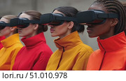 A stylish group dressed in vibrant outerwear engages with virtual reality headsets in a contemporary outdoor setting, demonstrating tech in fashion. Стоковое AI-видео, аниматор Данила Большаков / Фотобанк Лори