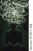 Person sitting in dimly lit room with abstract light patterns above head capturing thoughts in creative display. Стоковое AI-видео, аниматор Сергей Толмачёв / Фотобанк Лори