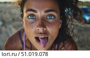 A young woman with stunning blue eyes and freckles expresses her playful side by sticking out her tongue as she relaxes outdoors. Стоковое AI-видео, аниматор Данила Большаков / Фотобанк Лори