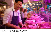 Butcher preparing fresh meat in a vibrant market setting during evening hours. Стоковое AI-изображение, AI-художник Сергей Толмачёв / Фотобанк Лори