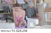 Young dressmaker cuts fabric in front of an experienced seamstress who checks a dress sample on a mannequin. Process of cutting fabric according to patterns and sewing clothes. Стоковое видео, видеограф Яков Филимонов / Фотобанк Лори